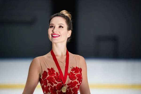 Happy figure skater in red dress and ribbon with golden medal — Stockfoto