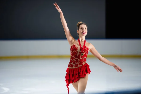 Positive figure skater in red dress and golden medal gesturing on ice arena — Stockfoto