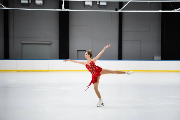 Comprimento total de patinador artístico em vestido vermelho realizando rotação de camelo na arena de gelo profissional — Fotografia de Stock