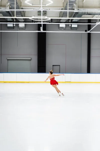 Full length of young woman in dress figure skating in frozen ice arena — Stock Photo