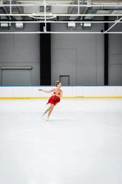 Повна довжина жінки в червоній сукні фігурне катання на професійній льодовій арені — стокове фото