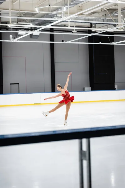 In voller Länge glückliche Frau im roten Kleid Eiskunstlauf mit ausgestreckten Händen in professioneller Eisarena — Stockfoto