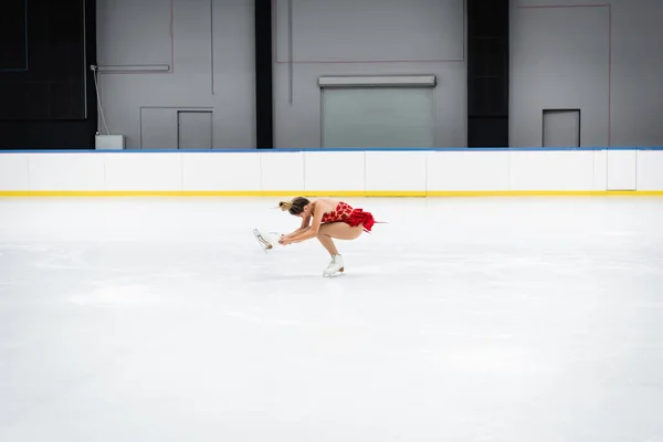 Pleine longueur de jeune femme en robe effectuer assis spin dans l'arène de glace professionnelle — Photo de stock