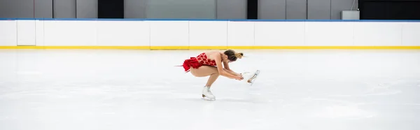 Full length of young woman in dress performing sit spin in professional ice arena, banner — Stock Photo