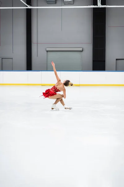 Full length of young woman with outstretched hand figure skating in professional ice arena — Stockfoto