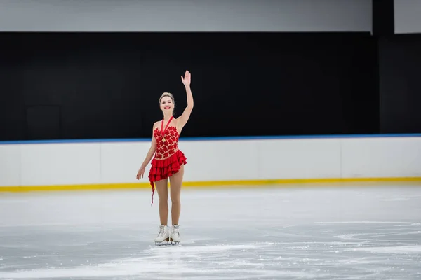 Pleine longueur de femme heureuse avec médaille agitant la main dans l'arène de glace professionnelle — Photo de stock