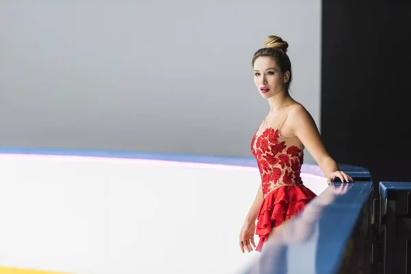 Young figure skater in red dress standing on ice rink — Stock Photo