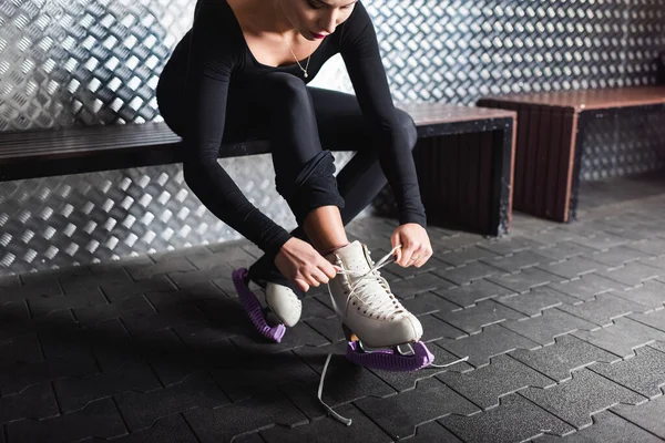 Mujer en traje de cuerpo atando zapatos de patinaje artístico mientras está sentado en el banco - foto de stock