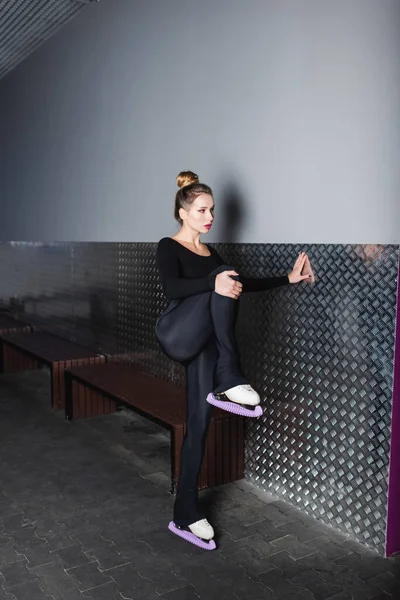 Full length of young woman in white figure skates stretching near wall — Stock Photo