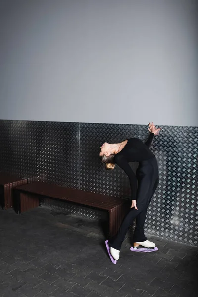 Longitud completa de la mujer joven en patines de figura blanca estiramiento y flexión cerca de la pared - foto de stock