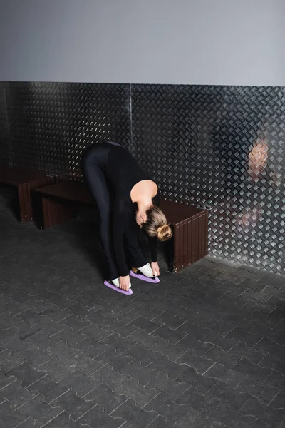 Full length of young woman in bodysuit and white figure skates stretching near wall — Stock Photo