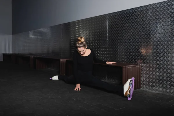 Full length of young woman in white figure skates doing splits near wall — Stock Photo