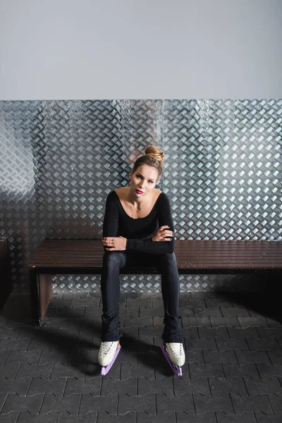 Longueur totale de la jeune femme en patins à roues alignées blancs et body noir assis sur le banc — Photo de stock
