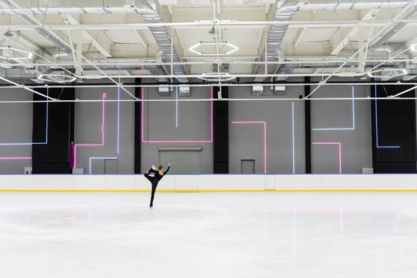 Back view of young woman in black bodysuit skating in professional ice arena — Stock Photo