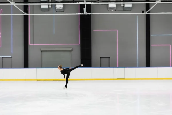 Side view of young woman in black bodysuit skating in professional ice arena — Stockfoto