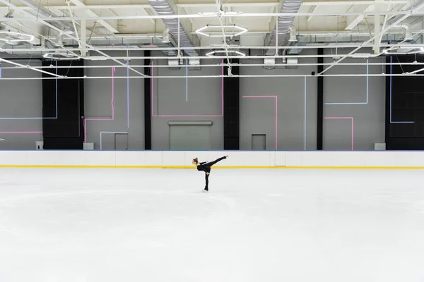 Vista lateral del patinador artístico en traje negro patinaje en arena de hielo profesional - foto de stock