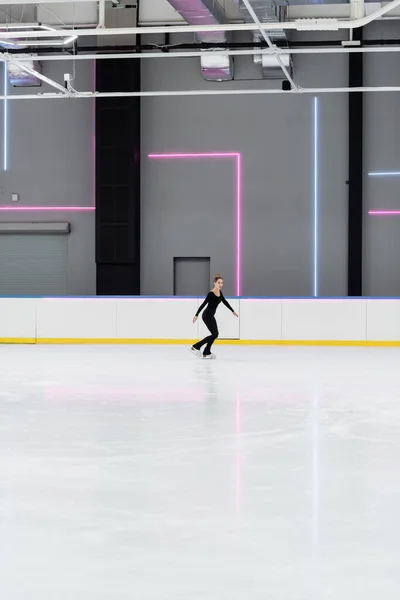 Full length of figure skater in black bodysuit skating in professional ice arena — Stock Photo