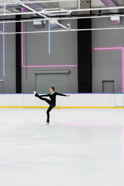 Toute la longueur du patineur artistique en costume de corps noir pratiquant dans l'arène de glace professionnelle — Photo de stock