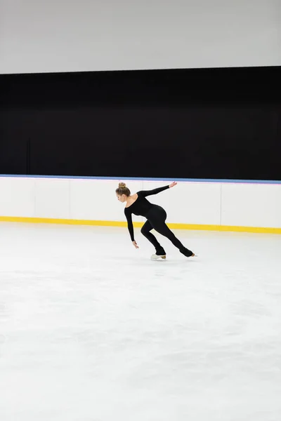 Full length of professional figure skater in black bodysuit skating in ice arena — Stock Photo