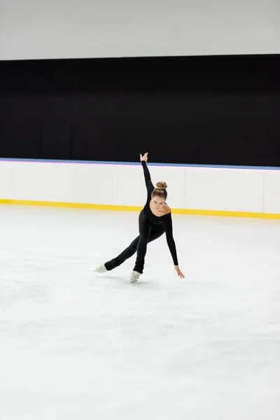 Full length of young professional figure skater in black bodysuit skating with outstretched hand in ice arena — Stock Photo