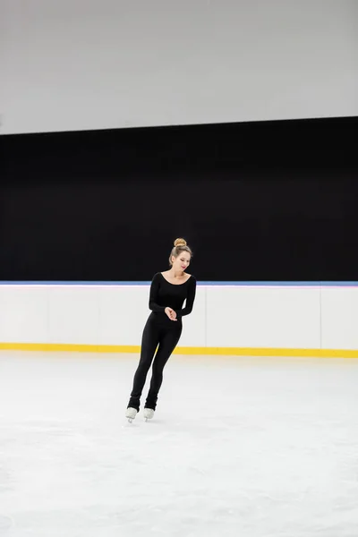 Longitud completa de patinador artístico profesional alegre en negro bodysuit patinaje en arena de hielo - foto de stock