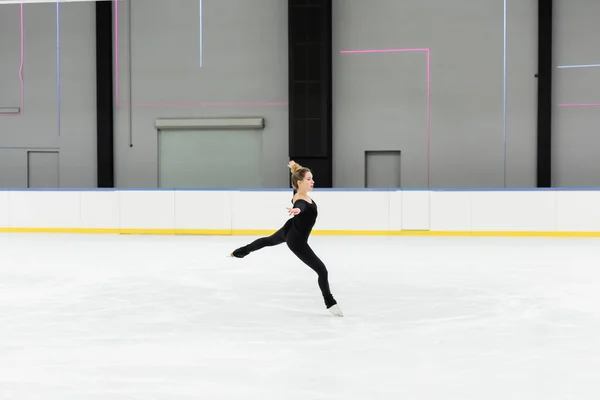 Full length of professional figure skater in bodysuit skating with outstretched hands in ice arena — Stock Photo