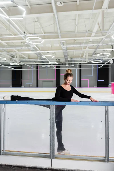 Young woman in white figure skates stretching near ice arena — Stock Photo