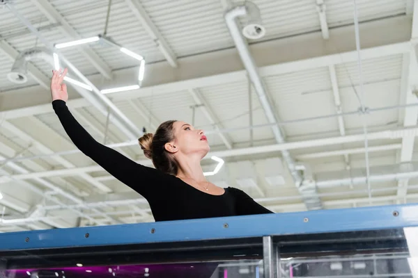 Low angle view of young woman in bodysuit stretching with raised hand — Stock Photo