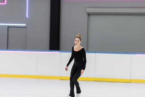 Toute la longueur du jeune patineur artistique en body noir patinant en patinoire — Photo de stock