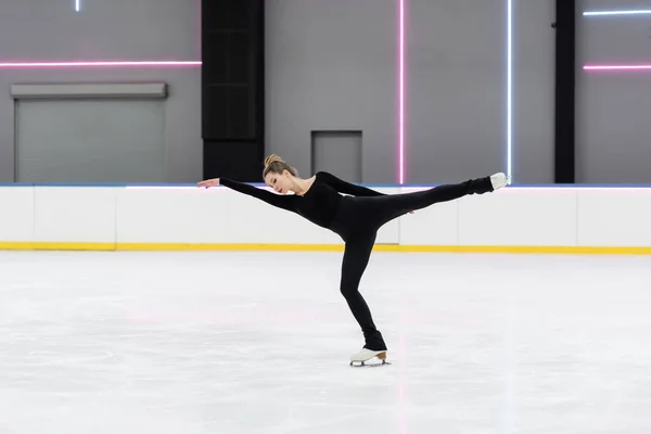 Full length of young figure skater in black bodysuit skating with outstretched hand in ice arena — Stock Photo