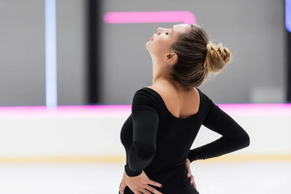 Worried figure skater with closed eyes in black bodysuit stretching back — Stock Photo