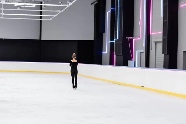 Visão traseira do jovem patinador artístico em bodysuit preto e patins de gelo na arena de gelo congelado — Fotografia de Stock