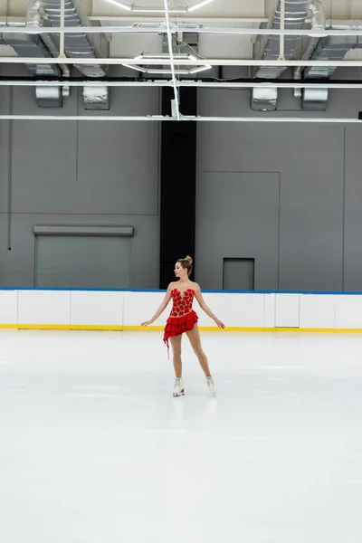 Full length of young figure skater in dress performing dance in professional ice arena — Foto stock