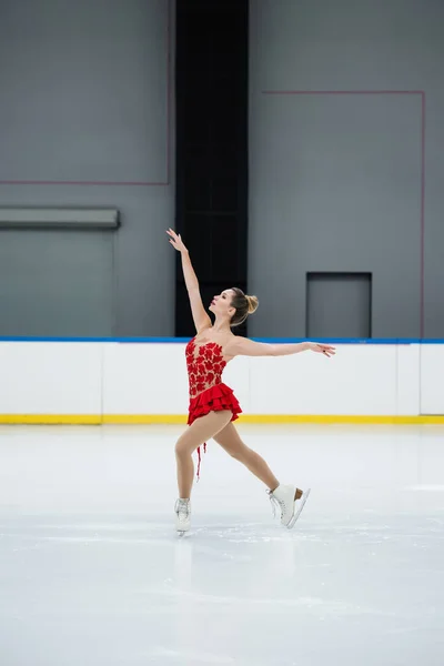 Comprimento total da mulher em patinação artística vestido vermelho com as mãos estendidas na pista de gelo profissional — Fotografia de Stock