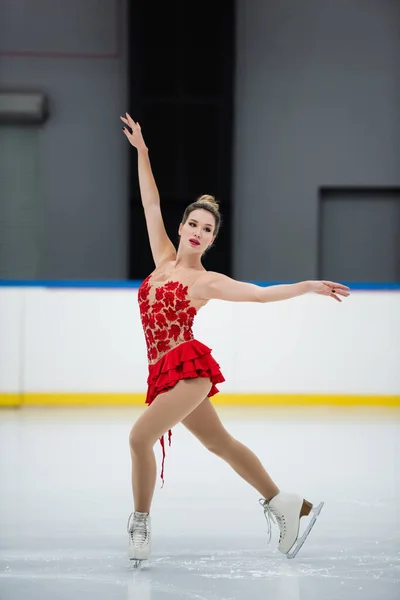 Full length of woman in red dress figure skating with outstretched hands on ice rink — Stockfoto