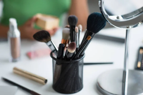 Cropped view of cosmetic brushes near mirror and blurred african american woman — Stock Photo