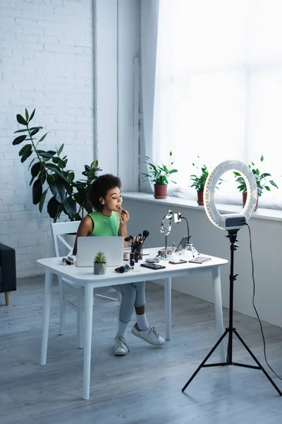 African american blogger applying lipstick near devices and ring light at home — Stock Photo