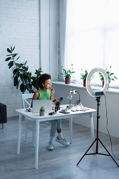 Blogger afroamericano aplicando lápiz labial cerca de dispositivos y luz de anillo en casa — Stock Photo