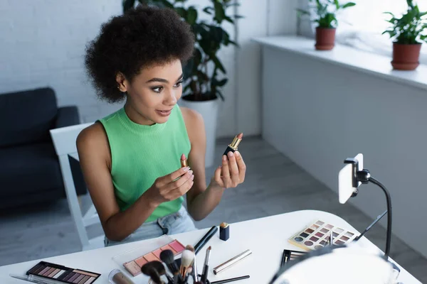 Afroamerikanische Bloggerin hält Lippenstifte in der Nähe ihres Smartphones zu Hause — Stockfoto