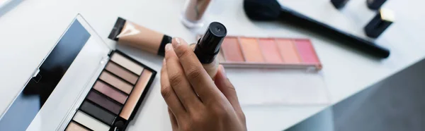 Vista recortada de la mujer afroamericana que sostiene la base de la cara cerca de cosméticos decorativos, pancarta - foto de stock