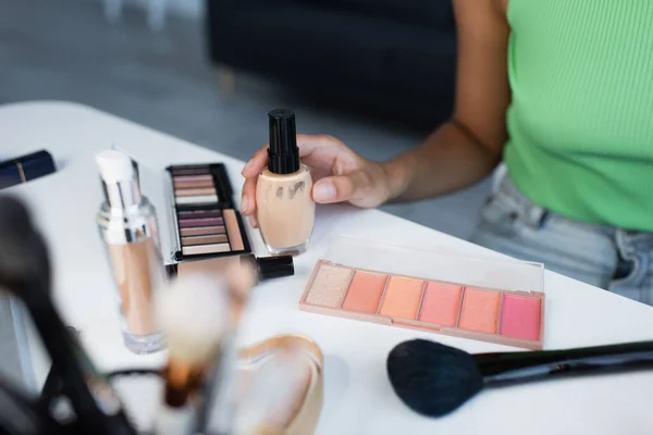 Vista recortada de cosméticos decorativos cerca de la mujer afroamericana en casa - foto de stock