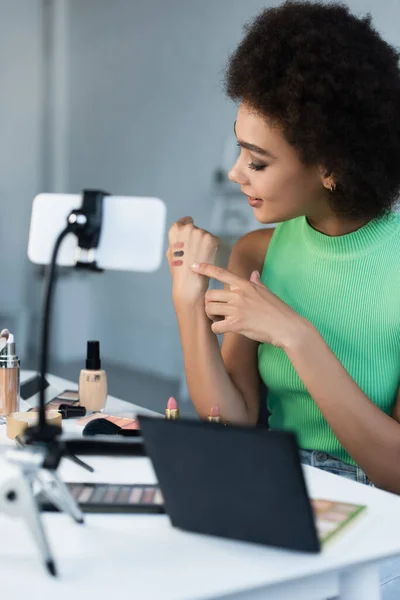 Positive blogger pointing at swatches of eye shadows near smartphone — Stock Photo