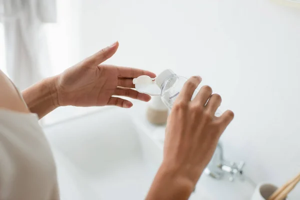 Cropped view of african american woman pouring lotion on cotton pad in bathroom — Foto stock