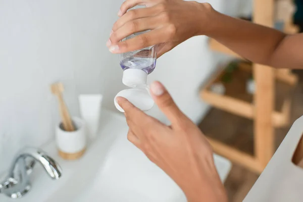 Cropped view of african american woman pouring lotion on cotton pad near sink in bathroom — Stock Photo