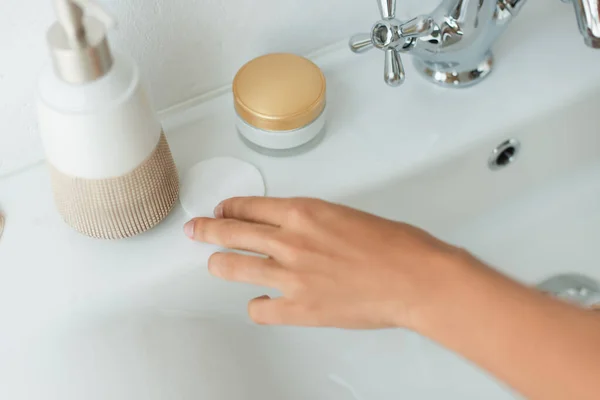 Ausgeschnittene Ansicht einer afrikanisch-amerikanischen Frau, die Baumwollpolster aus dem Waschbecken im Badezimmer nimmt — Stockfoto