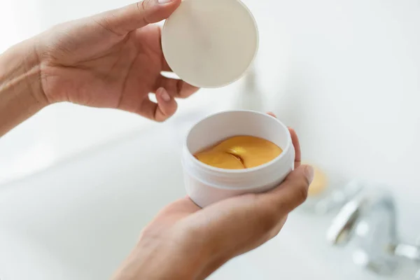 Vue recadrée d'une femme afro-américaine tenant un pot avec des patchs hydrogel dans la salle de bain — Photo de stock