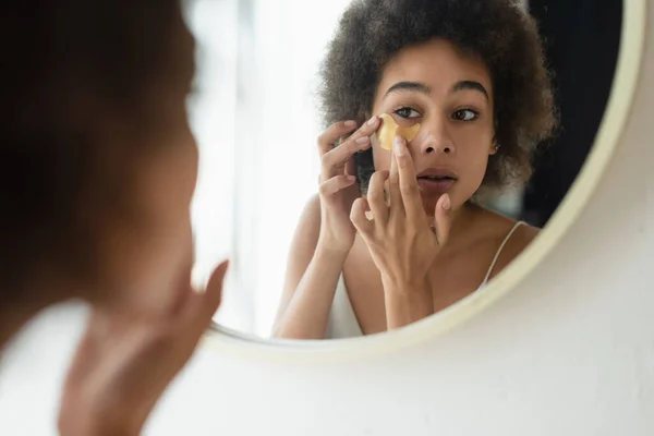 Young african american woman applying eye patch near mirror in bathroom — Stock Photo
