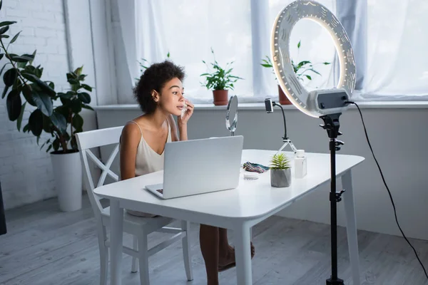 African american blogger wiping face with napkin near gadgets and ring light at home — Stockfoto
