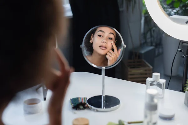 Unscharfe afrikanisch-amerikanische Frau Anwendung kosmetischer Creme in der Nähe von Spiegel und Parfüm zu Hause — Stockfoto