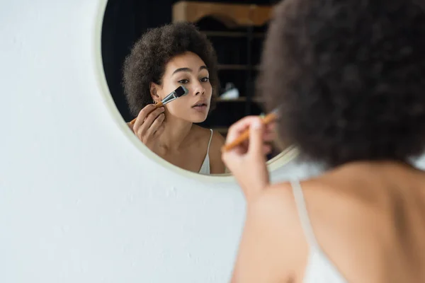 Donna afroamericana offuscata applicare maschera di argilla sul viso vicino specchio in bagno — Foto stock